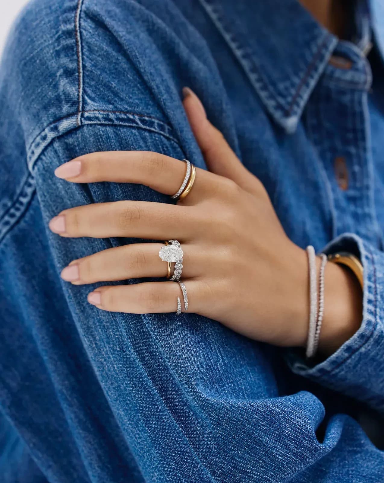 The ring stacked with others, hand against denim